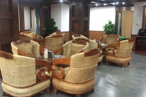 Une pièce meublée de mobilier en osier disposé autour d’une table centrale, avec des murs en bois et une plante en arrière-plan.