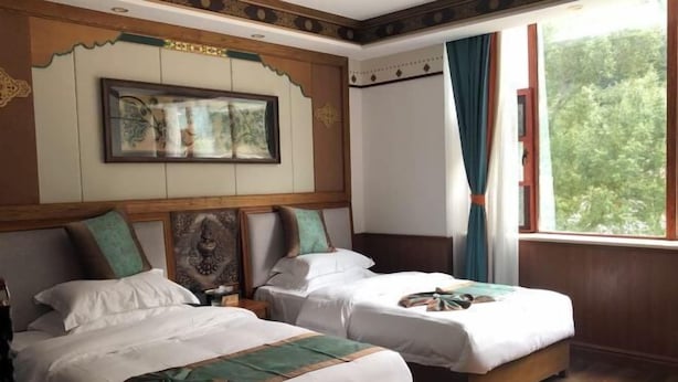 Quarto de hotel com duas camas, uma janela grande com cortinas, uma obra de arte emoldurada acima das camas e piso de madeira.