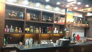 Uma área de bar com prateleiras cheias de garrafas e bules, um balcão com copos e objetos decorativos.