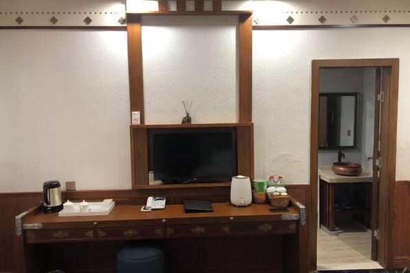 Hotelkamer met een houten bureau, een flatscreen televisie, een koffiezetapparaat, een telefoon en een kleine plant.