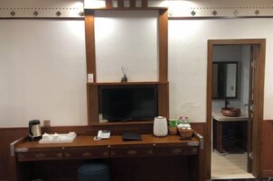 Habitación de hotel con escritorio de madera, televisor de pantalla plana, cafetera, teléfono y una planta pequeña.