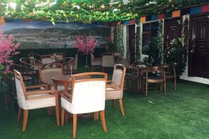 Un espace extérieur aménagé avec des tables et des chaises, entouré de verdure et agrémenté d’une fresque murale.