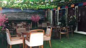 Un espace extérieur aménagé avec des tables et des chaises en bois, entouré de verdure et orné d’une fresque représentant un paysage urbain.