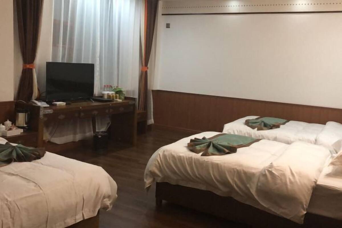 Ein Hotelzimmer mit zwei Betten, einem Schreibtisch mit Fernseher und einem Fenster mit Vorhängen.