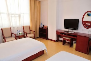 A hotel room with two beds, a desk with a TV, a chair, a small table with a bottle, and a window with curtains.