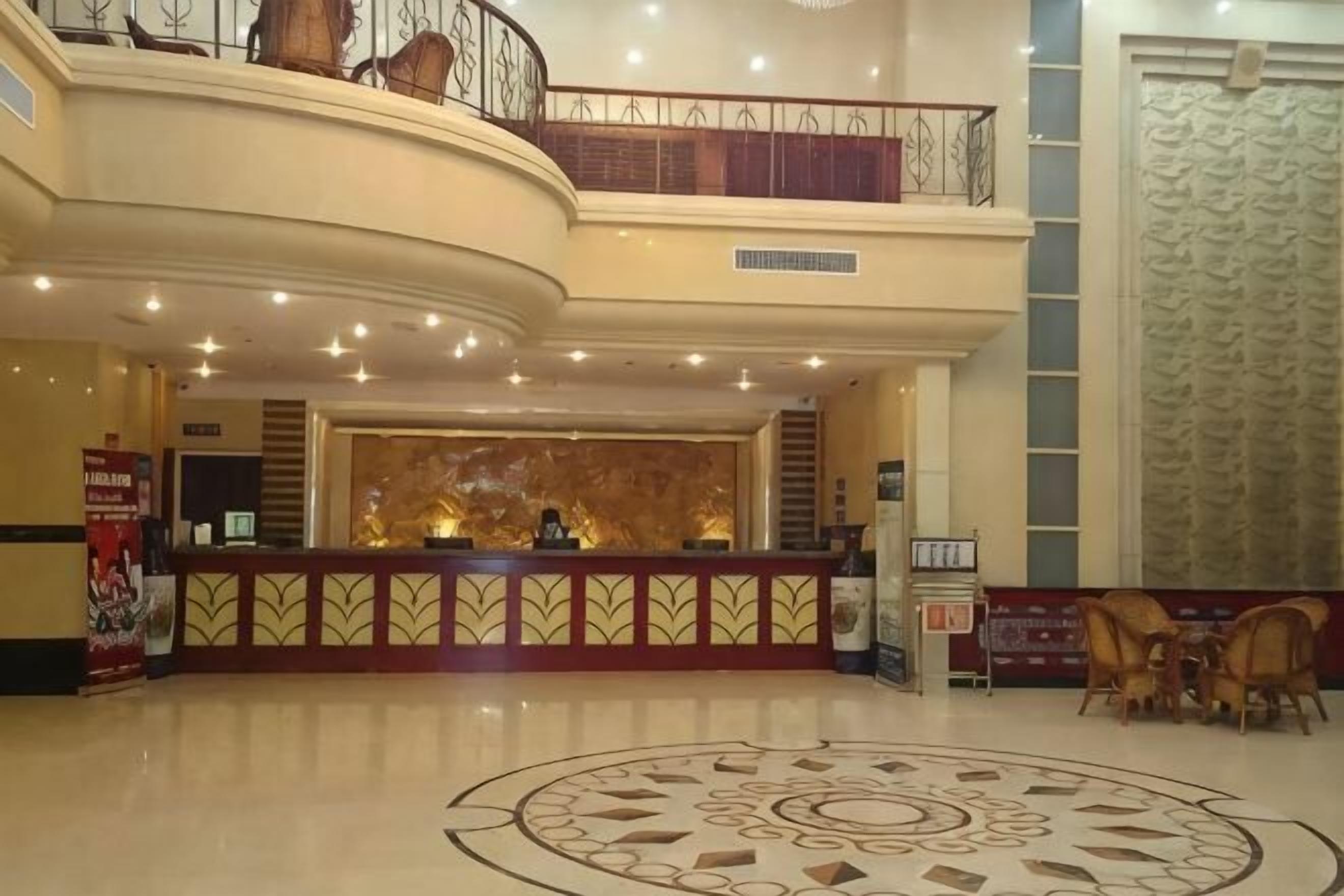 A hotel lobby with a reception desk, a decorative circular floor pattern, a staircase, and a large window with a patterned curtain.. Hongxiang Hotel