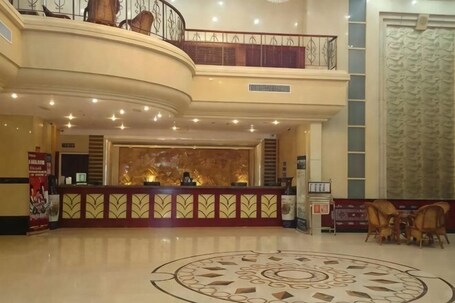 A hotel lobby with a reception desk, a decorative circular floor pattern, a staircase, and a large window with a patterned curtain.. Hongxiang Hotel