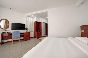 A hotel room with a bed, a desk with a chair, a television, a wardrobe, and a mirror. - Hongxiang Hotel (Linyi)