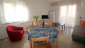 A dining area with a round table, chairs, a red sofa, a television, and a refrigerator. - Apartment Branka for 2 -3 person (Premantura)