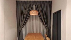 A dining area with a wooden table and chairs, a hanging light fixture, and grey curtains. - Bali Service Residence•WiFi 500Mbps (Melaka)