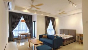 A modern living room with a sofa, ottoman, dining table, and chairs. There is a bed with a headboard and a ceiling fan. - Bali Service Residence•WiFi 500Mbps (Melaka)