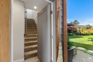 A staircase leading to a door, a wooden exterior wall, and a garden with grass and plants.