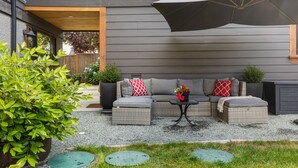 A modern outdoor seating area with a grey sofa, ottoman, and a table with a potted plant.