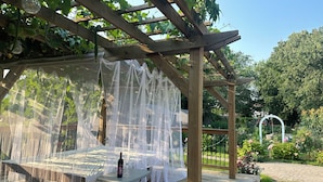 Una pergola in legno con tavolo e sedie, ricoperta da una rete bianca.