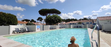 A pool area with clear blue water, lounge chairs, and a tiled deck.