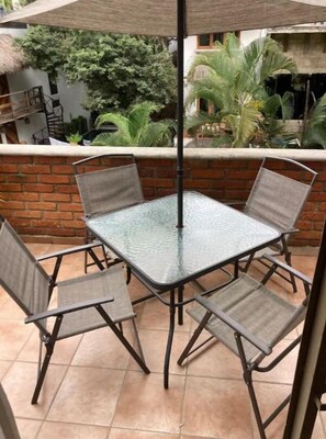 An outdoor patio with a glass table and four chairs, surrounded by a brick wall and plants. - Sayulita - Spacious 1 BR - Walk to Town and Beach (Sayulita)