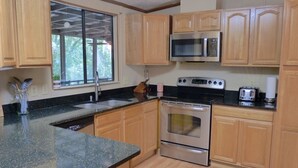 Una cocina con armarios de madera, horno de acero inoxidable, microondas, tostadora y ventana con vista a zonas verdes.