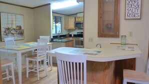 Una cocina moderna con armarios blancos, una isla central y un comedor con sillas blancas.