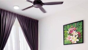Une chambre d’hôtel avec un lit, un ventilateur de plafond, une fenêtre avec des rideaux et un tableau floral accroché au mur.
