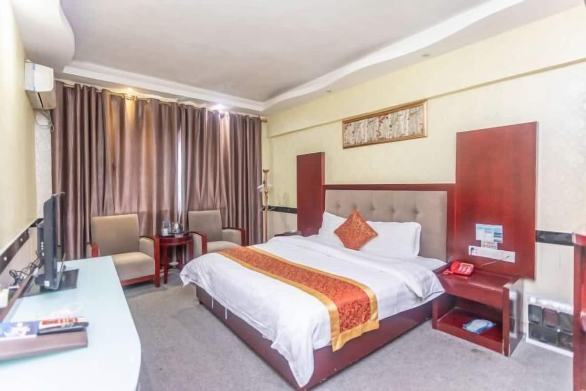 A hotel room with a bed, a desk, a chair, a TV, and a red telephone.