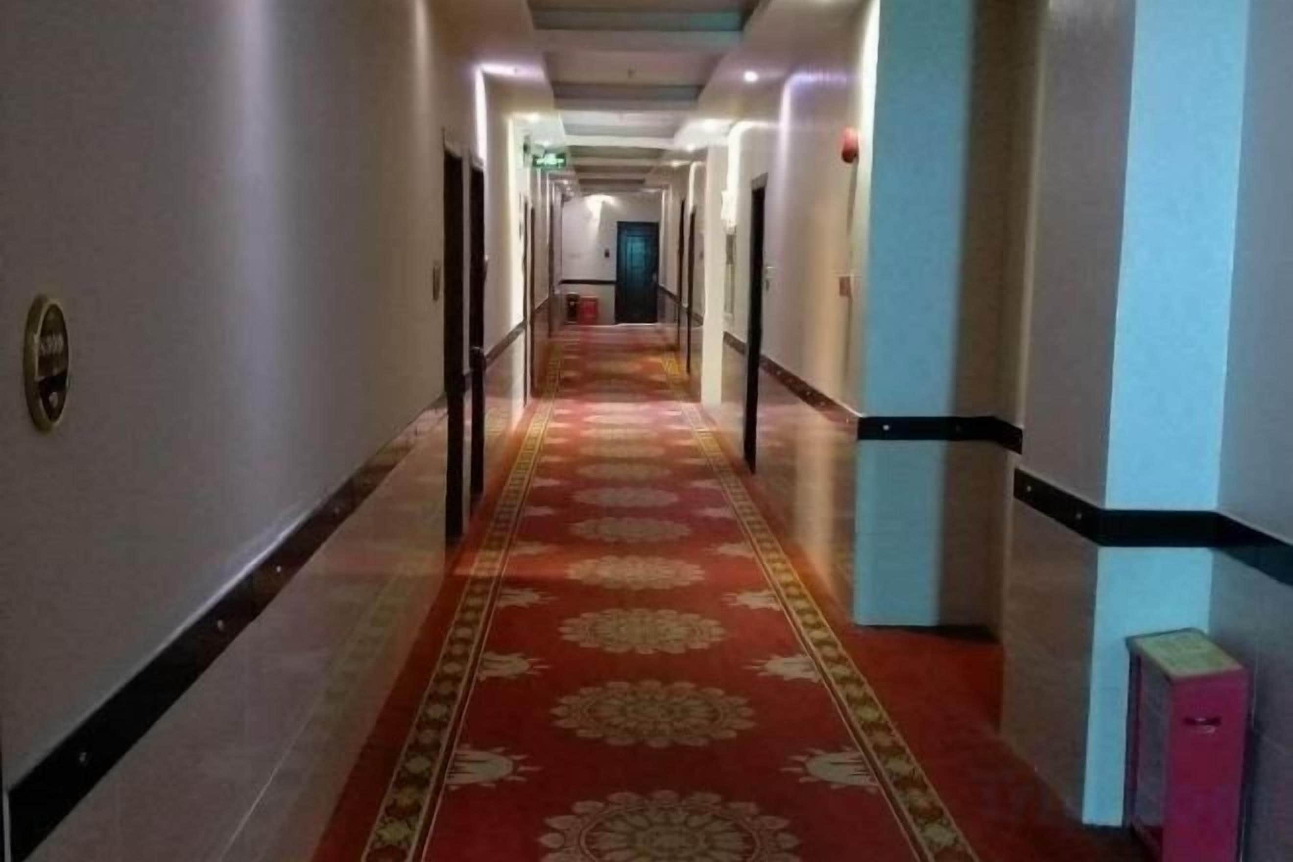 Hotelgang med rødt tæppe, døre på begge sider og en blå væg til højre.