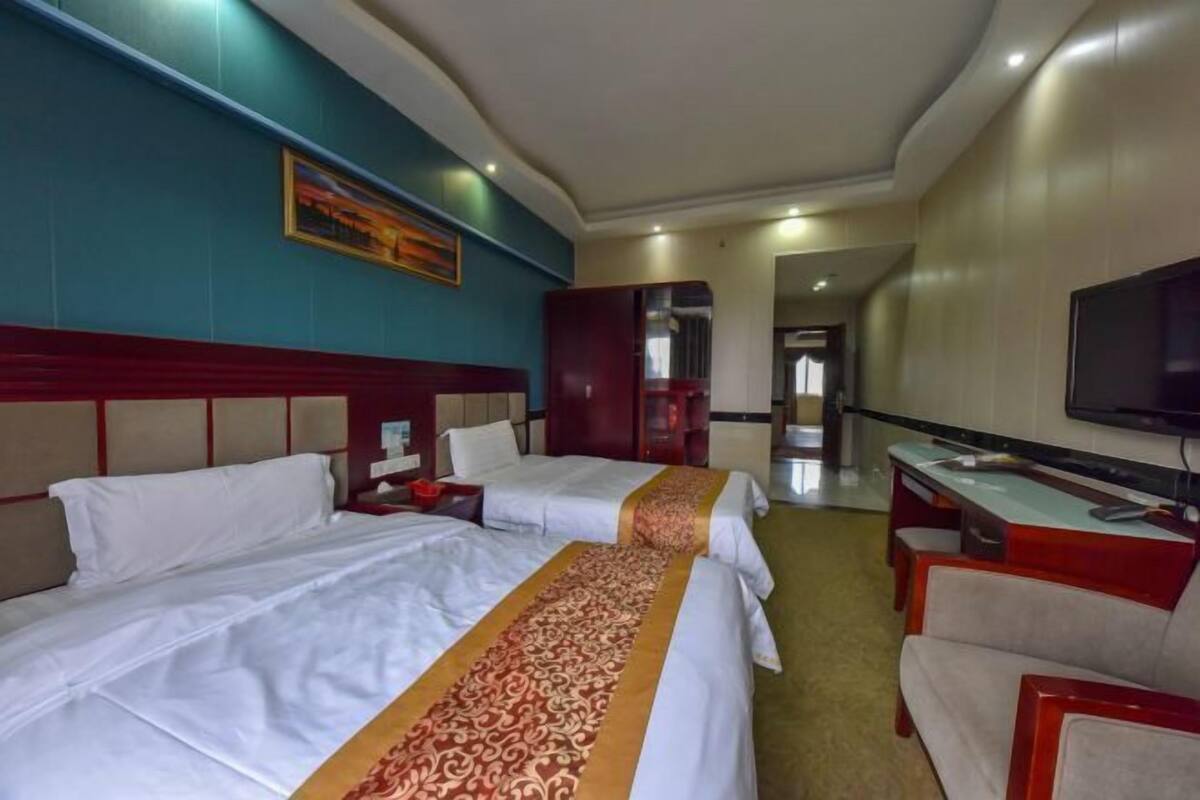 A hotel room with two beds, a desk, a TV, and a door leading to a hallway.