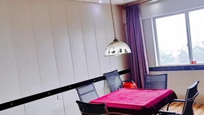 A dining area with a table covered in a pink tablecloth, black chairs, a hanging pendant light, and a window with curtains. - Mindu Hotel (Shenzhen)