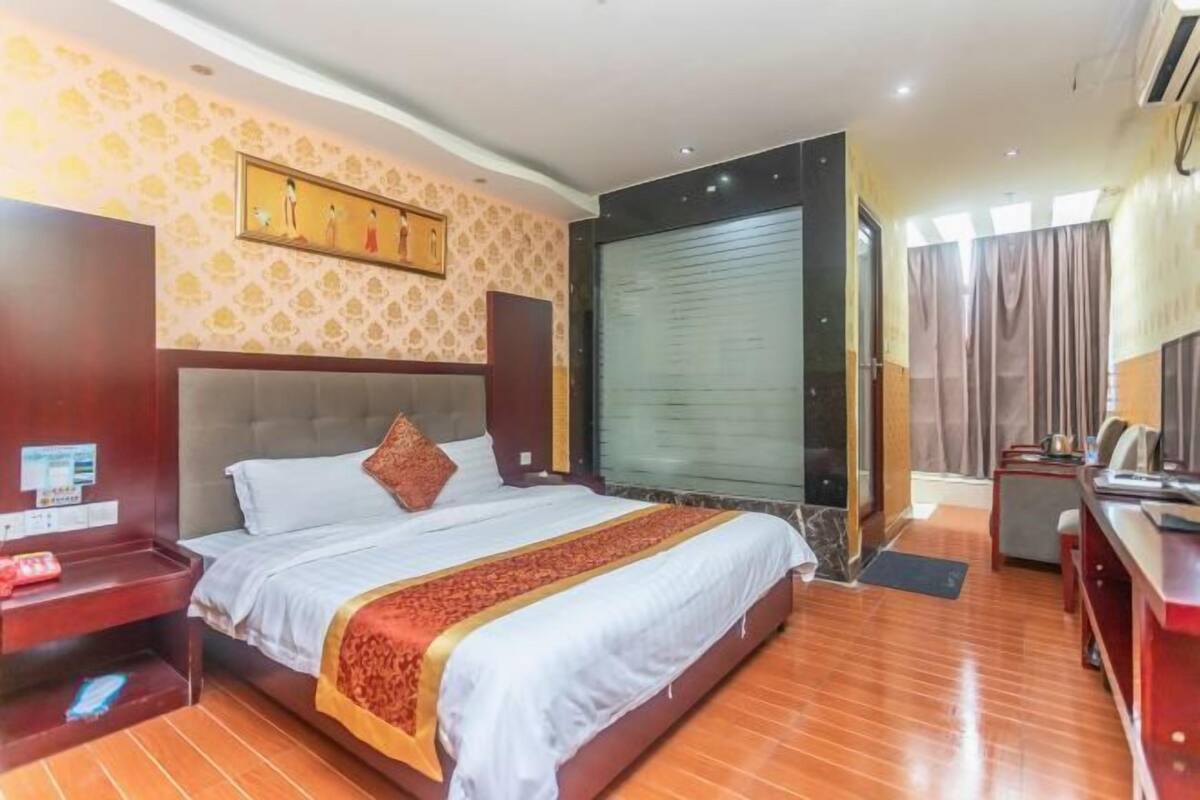 A hotel room with a large bed, a desk, a chair, a wardrobe, and a window with curtains.