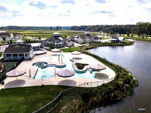 A resort with a large swimming pool, multiple umbrellas, and a lake view.