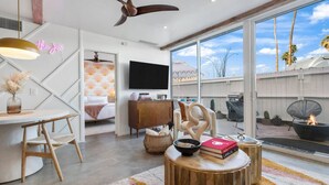 A modern living room with a large TV, a dining area with a wooden table, and a cozy seating area with a fire pit. - Boho chic condo at the mid-century Ocotillo Lodge (Palm Springs)