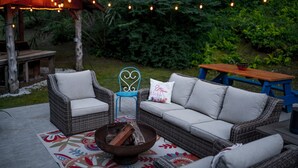 Zona relax all'aperto con mobili in vimini, un braciere e luci decorative.