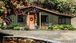 A rustic cabin with a stone entrance, a wooden door, and a porch with outdoor seating. - Appalachian hideaway (Franklin)