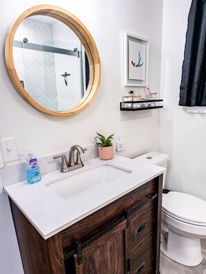 A bathroom with a white sink, wooden vanity, a round mirror, a framed artwork, and a toilet. - Appalachian hideaway (Franklin)