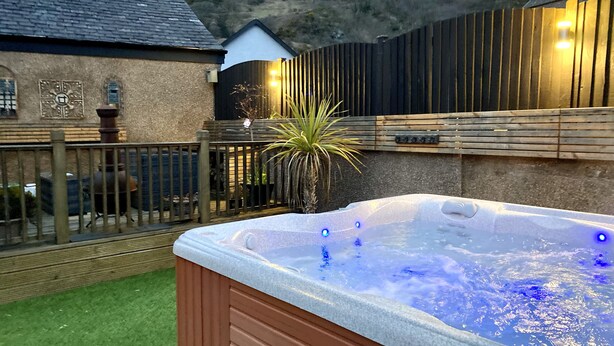 Un jacuzzi en un patio trasero con una valla de madera y una casa al fondo.