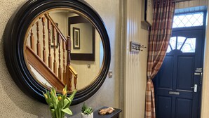 Un pasillo con un espejo grande, una escalera de madera, una puerta oscura y una pequeña consola con plantas.