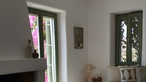 Een woonkamer met een open haard, een bank, een salontafel en uitzicht op de natuur door een raam.