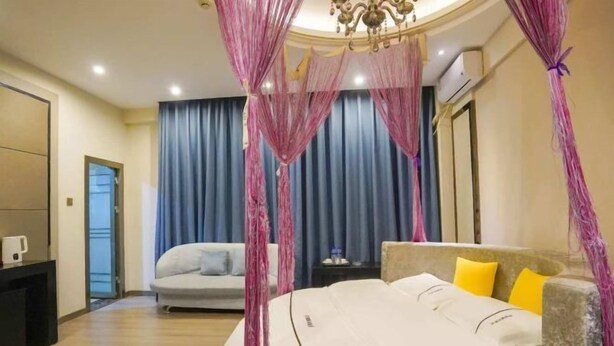 A hotel room with a bed, a nightstand, a desk, a chair, a sofa, a chandelier, and curtains.
