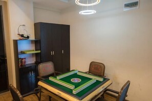 A room with a table set for a game, two chairs, a dark cabinet, and a ceiling light fixture. - Gui Gui Jia Ri Hotel (Jianshui)