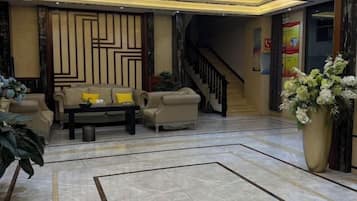 Um hall de entrada com um conjunto de sofás, uma mesa de centro, um vaso grande com flores e uma escadaria ao fundo.