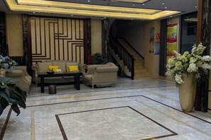 A lobby with a sofa set, a coffee table, a large vase with flowers, and a staircase in the background. - Gui Gui Jia Ri Hotel (Jianshui)