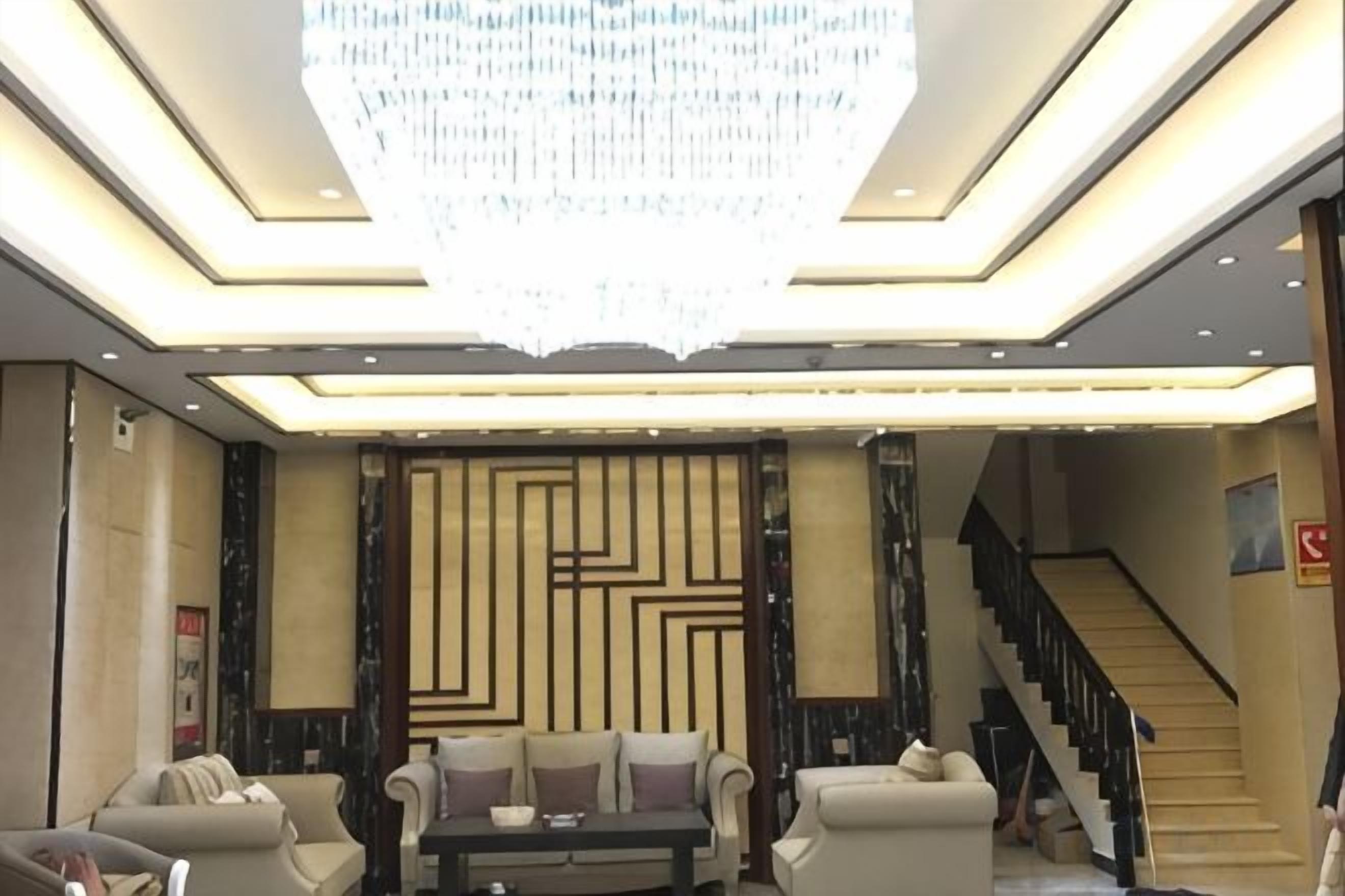 A hotel lobby with a chandelier, sofas, a coffee table, and a staircase.