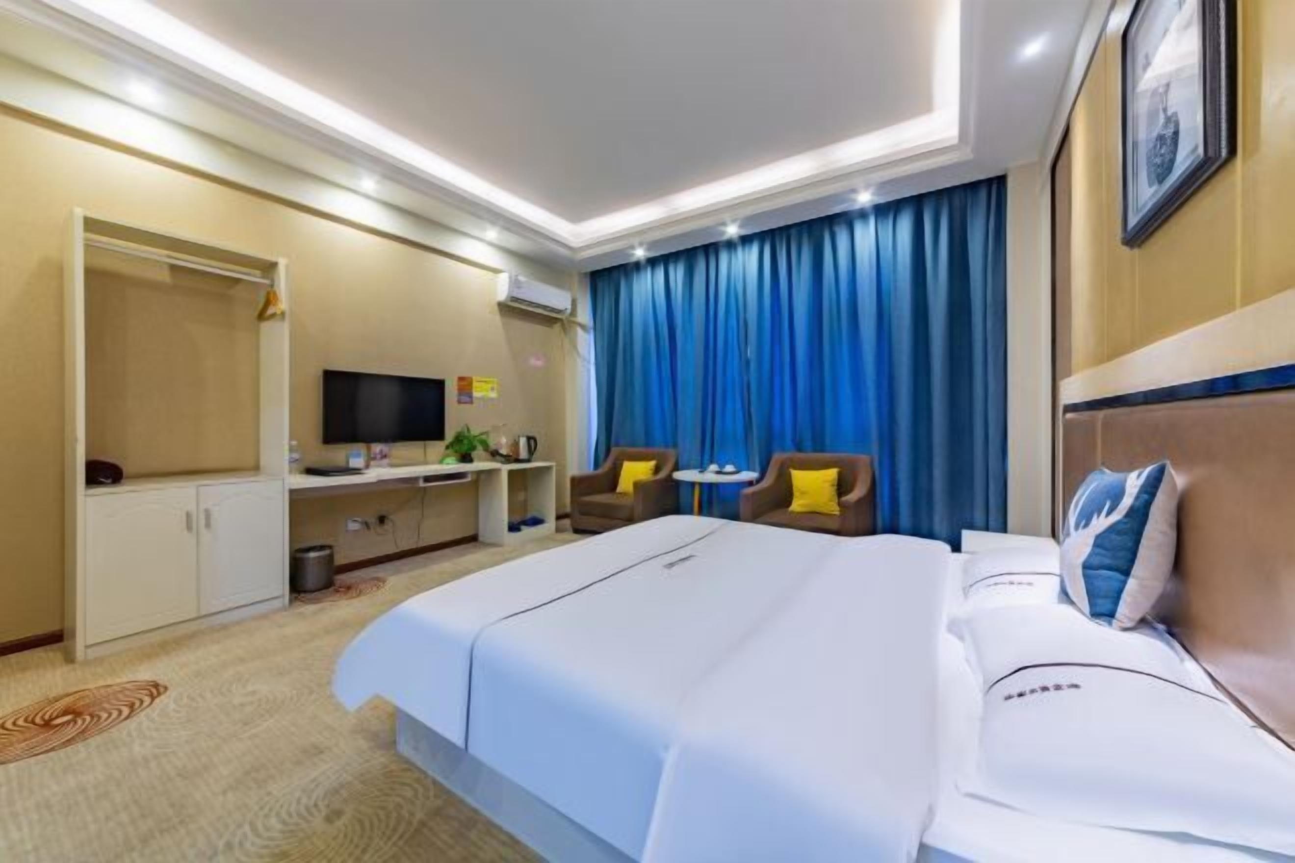 A hotel room with a large bed, a desk with a TV, a chair, and a blue curtain.
