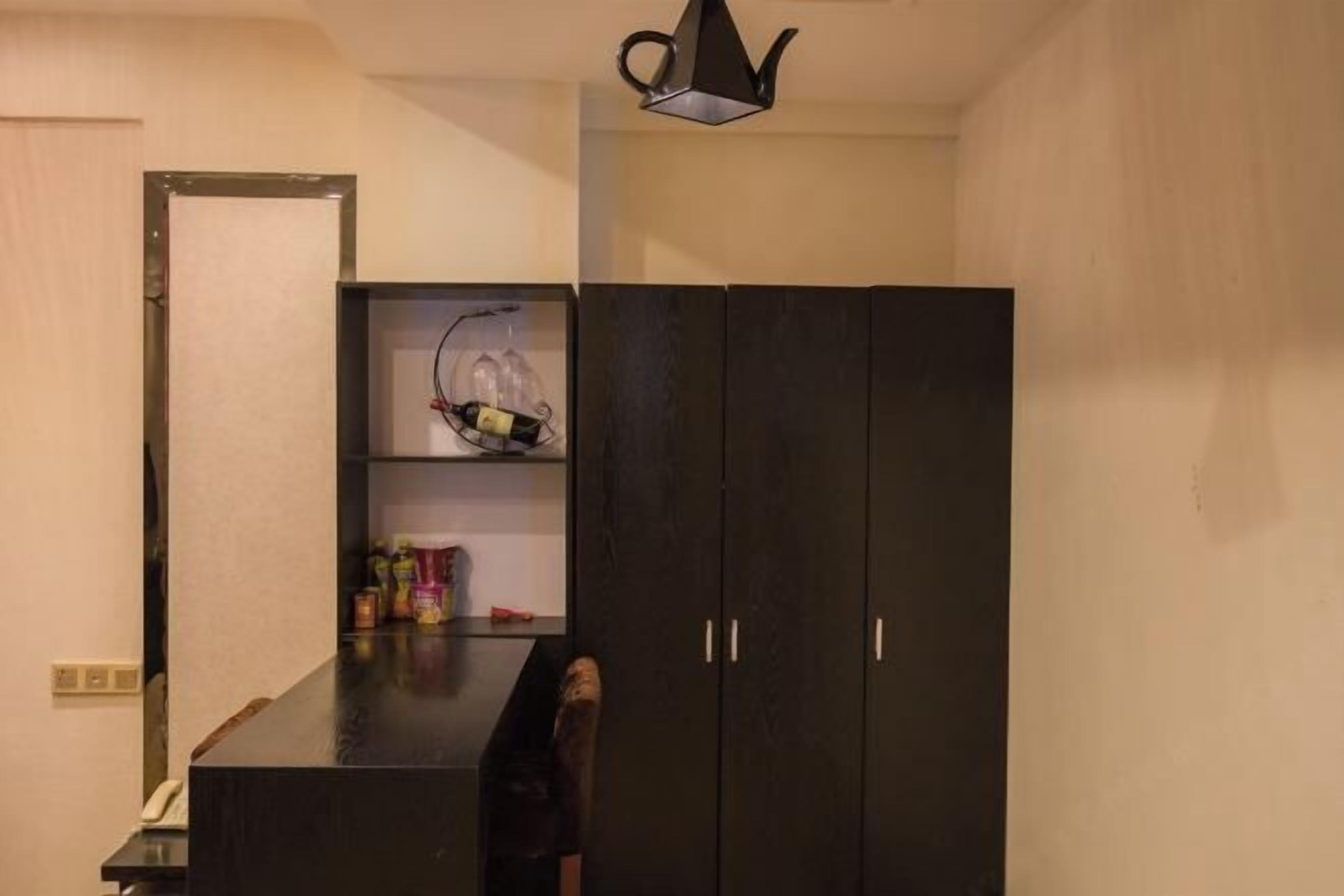 A compact room with a dark wooden wardrobe, a small shelf with bottles, and a chair.