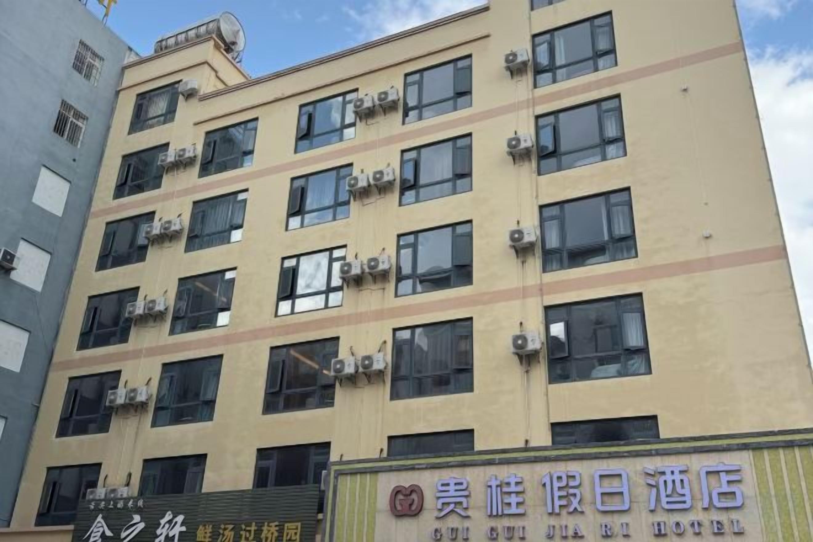 A multi-story hotel building with air conditioning units on the facade, a signboard with hotel name, and a visible entrance.