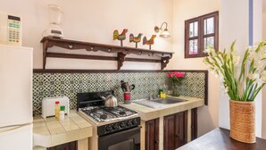 A kitchen with a gas stove, a toaster, a blender, and a sink. There are decorative wall tiles and a window with curtains. - Casita El Mirador  (Antigua Guatemala)