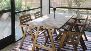 Eine überdachte Terrasse mit Tisch, Stühlen, großen Fenstern und einem Deckenventilator.