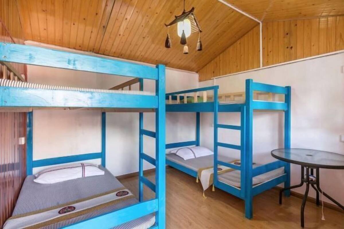 A room with bunk beds, a small round table, and a wooden ceiling.