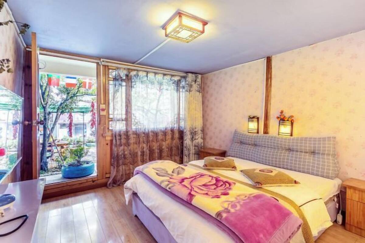 A bedroom with a bed, bedside tables, a window with curtains, and a ceiling light fixture.