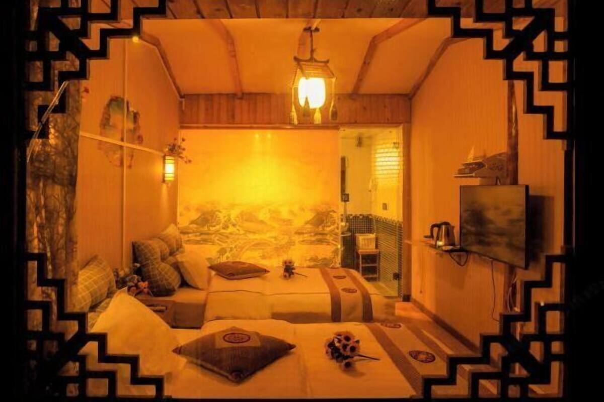 A room with two beds, a wall-mounted TV, a wooden ceiling, and a patterned wall.