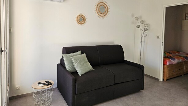 A modern living room with a black sofa, two decorative wall mirrors, a standing lamp, and a ceiling-mounted air conditioner.